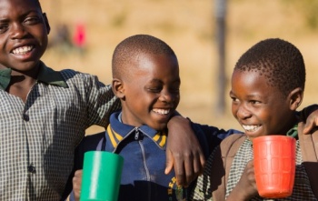 Image of three boys holding mugs with their arms over each other's shoulders.