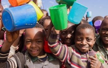 Large group of children holding their mugs in the air and smiling.