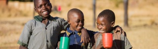 Image of three boys holding mugs with their arms over each other's shoulders.