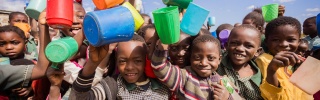 Large group of children holding their mugs in the air and smiling.