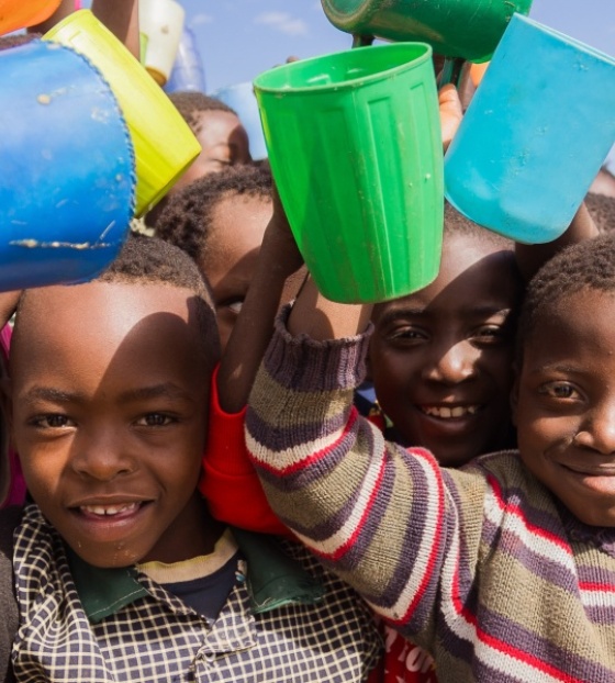 Large group of children holding their mugs in the air and smiling.