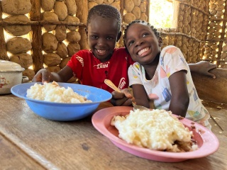 Two children with plates of food sitting at a table smiling.