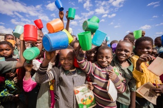 Large group of children all holding their mugs in the air and smiling into the camera.